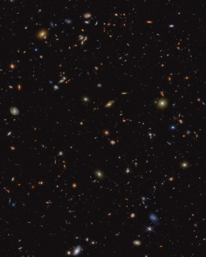 Thousands of small galaxies are scattered on a black background. Some are noticeably spirals, either face-on or edge-on, while others are blobby ellip…
