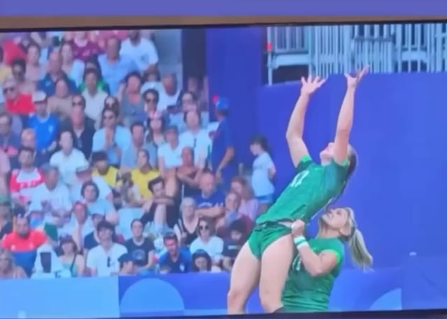 Woman on the Ireland Rugby team picking up one of her teammates to catch the ball